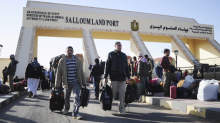 Egyptians cross from Libya to Egypt through the Salloum land port gate, background,Tuesday, Feb. 22, 2011. An estimated 5,000 Egyptians have returned home from Libya by land, and about 10,000 more are waiting to cross the Libya-Egypt border, an Egyptian security official said.